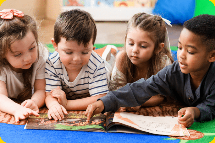 Four children lying on the floor reading a book together.