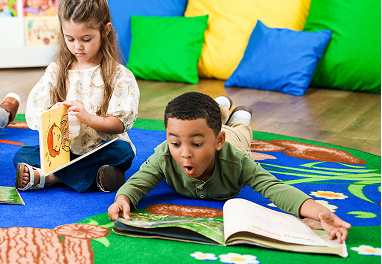 A boy reading a book while lying on the floor in a classroom.