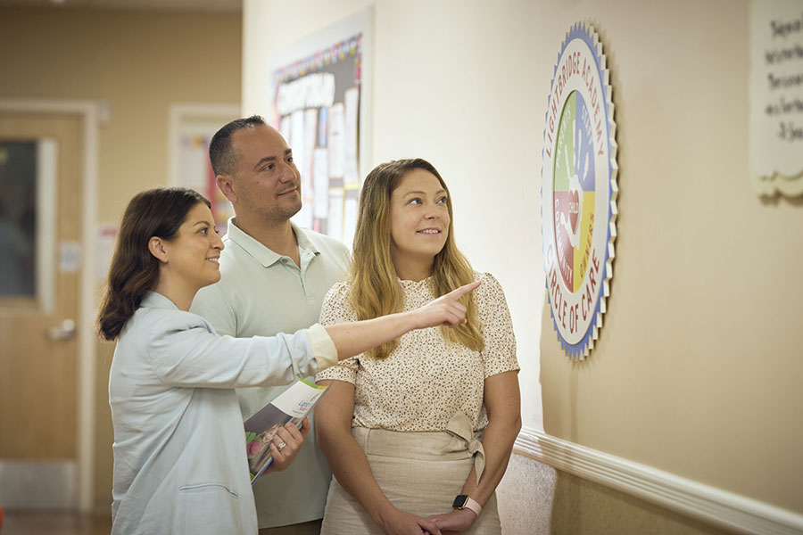 Three People Looking at Lightbridge Academy Logo on Wall