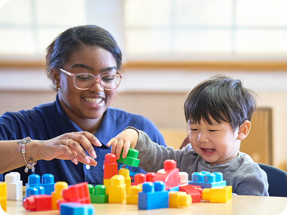 A teacher and a child playing with blocks while seated at a table.