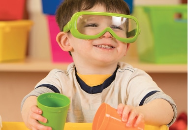 A preschool aged child wearing safety goggles and holding two cups.
