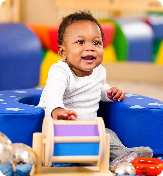 A baby playing with a toy seated on the floor.