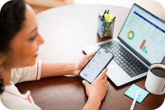A mother looking at a laptop and smartphone while sitting at a desk.