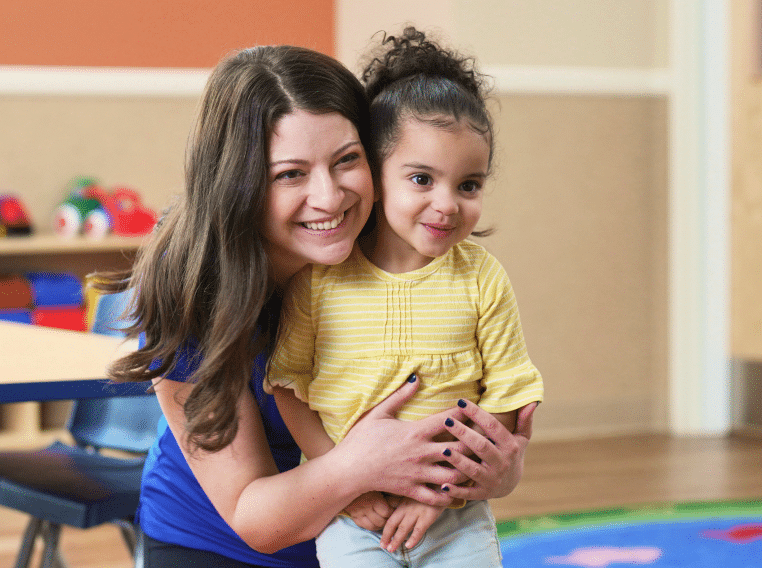 A preschool teacher hugging a young child.
