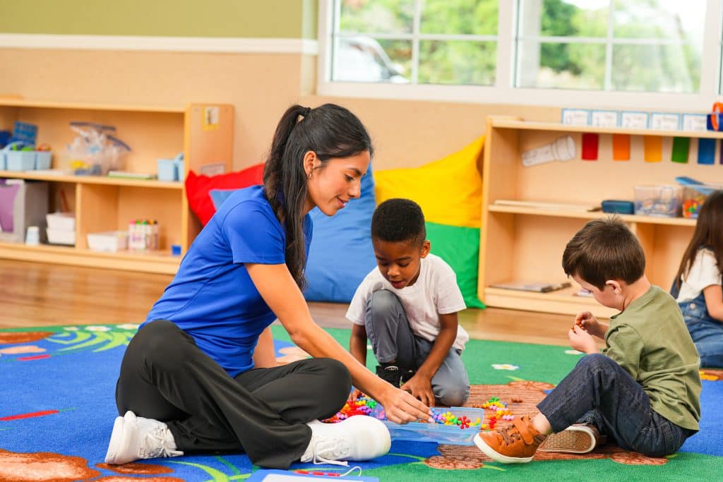 A teacher playing with two students in a preschool classroom.