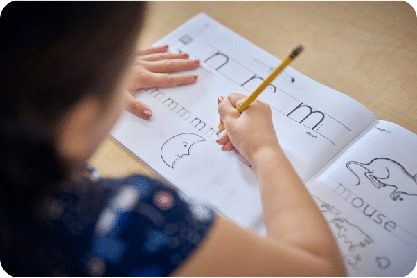 A child's hand holding a pencil and working on writing the letter m.