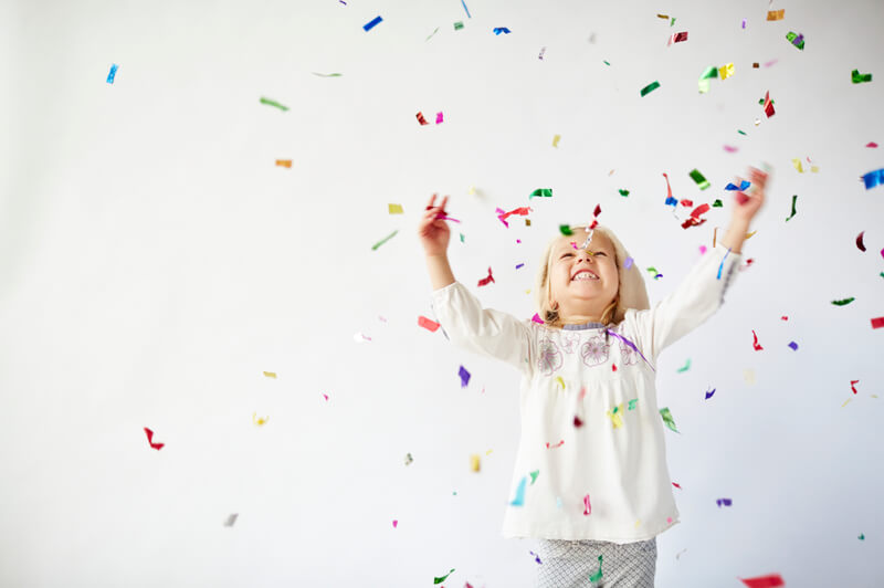 Young child surrounded by confetti, smiling and playing for the new year