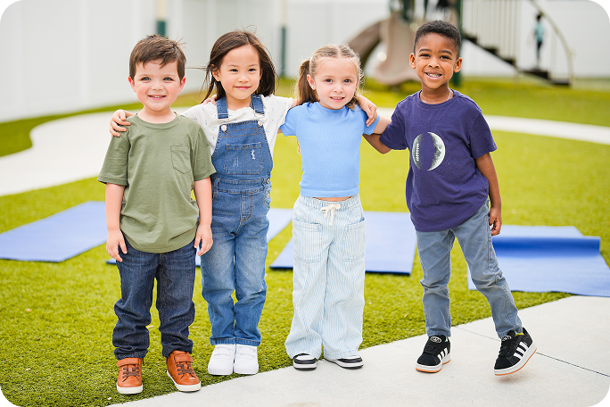 Four preschool children with their arms around each other on a playground.