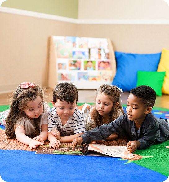 Four children reading a book while lying on a rug in a classroom.