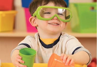 A preschool aged child wearing safety goggles and holding two cups.